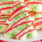 Homemade Christmas Tree Cakes coated in white chocolate with red drizzle and green sprinkles on a festive holiday plate.