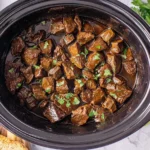 Slow Cooker Steak Bites cooked in rich gravy inside a slow cooker, garnished with fresh parsley and served warm