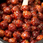 Close-up of Cranberry BBQ Crockpot Meatballs coated in a thick, glossy cranberry barbecue sauce inside a slow cooker