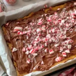 Gluten Free Christmas Crack topped with melted chocolate and crushed candy canes on a baking sheet.