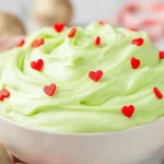 Creamy Grinch Dip topped with red heart sprinkles in a white bowl, festive holiday dessert.