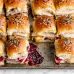 Freshly baked Turkey Cranberry Sliders with layers of turkey, melted cheese, and cranberry sauce on buttery rolls topped with everything seasoning.