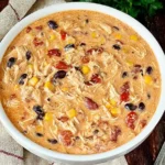 Creamy Crock Pot Cream Cheese Chicken Chili in a white bowl with shredded chicken, beans, corn, and tomatoes on a rustic table.