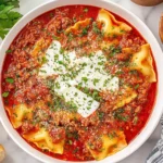 Bowl of Crockpot Lasagna Soup topped with ricotta, parmesan, and fresh herbs, served with bread on the side.