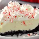 Slice of creamy White Chocolate Peppermint Pie topped with whipped cream and crushed peppermint in a chocolate cookie crust.