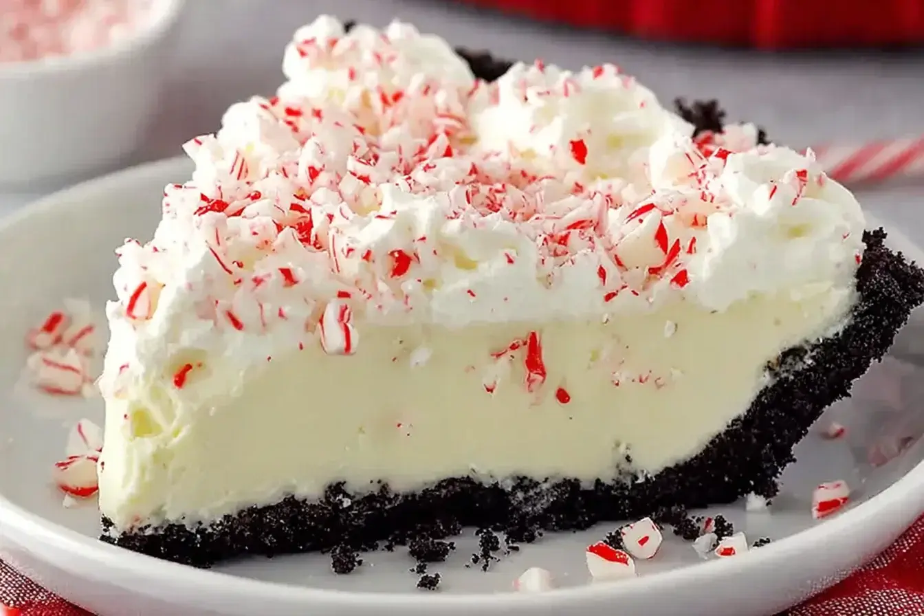 Slice of creamy White Chocolate Peppermint Pie topped with whipped cream and crushed peppermint in a chocolate cookie crust.