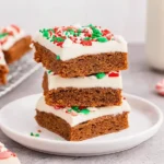 Stack of frosted Chewy Gingerbread Bars topped with festive red and green sprinkles on a white plate.