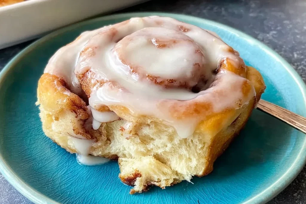 Gluten Free Cinnamon Rolls with a soft, fluffy center and creamy icing, served warm on a blue plate with a bite taken out