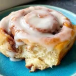 Gluten Free Cinnamon Rolls with a soft, fluffy center and creamy icing, served warm on a blue plate with a bite taken out
