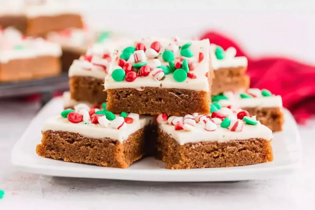 Holiday Chewy Gingerbread Bars topped with cream cheese frosting and festive red and green sprinkles on a white plate.