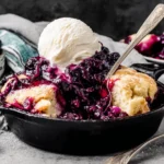 Blackberry Dumplings served warm in a cast iron skillet with vanilla ice cream and sweet blackberry sauce