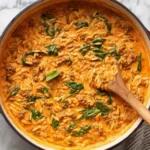 Ground Beef Orzo with Tomato Cream Sauce cooking in a red Dutch oven with spinach