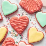 Red Velvet Sugar Cookies in heart shapes decorated with pastel icing and drizzle on a marble surface