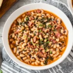 Slow Cooker Black-Eyed Peas Recipe served in a white bowl with bacon, greens, and cornbread on the side