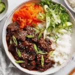 Slow Cooker Korean Beef Recipe bowl with rice, shredded carrots, cucumbers, and scallions