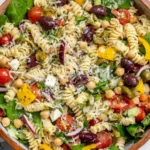 Italian Pasta Salad in a rustic bowl with fusilli, chickpeas, cherry tomatoes, spinach, kalamata olives, pepperoncini, and shaved Parmesan