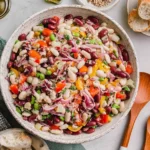 Italian Grinder Bean Salad in a large bowl with kidney beans, white beans, peppers, red onion, and herbs on a light tabletop.