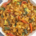 Drunken Noodles (Pad Kee Mao) with wide rice noodles, chicken, broccoli, red bell peppers, and Thai basil in a savory glossy sauce.