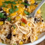 Close-up serving of Southwest Crock Pot Chicken and Rice with shredded chicken, white rice, black beans, corn, melted cheddar, cilantro, and lime.
