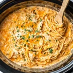 Creamy Crock Pot Chicken Spaghetti in a slow cooker with shredded chicken, spaghetti noodles, melted cheddar, and parsley.