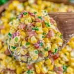 Creamy Crack Corn Salad with sweet corn, crispy bacon, cheddar, and fresh herbs on a wooden spoon.