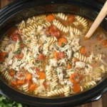 Crockpot Italian Chicken Soup with shredded chicken, rotini pasta, carrots, and tomatoes in a slow cooker