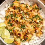 Thai Peanut Chicken over fluffy white rice with creamy coconut peanut sauce, chopped peanuts, cilantro, and fresh lime wedges.