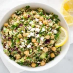 The Jennifer Aniston Salad in a white bowl with quinoa, chickpeas, cucumber, red onion, fresh herbs, feta, and lemon slices.
