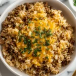 Cheesy Ground Beef and Rice Casserole in a bowl topped with melted cheddar cheese and fresh parsley, photographed from above.