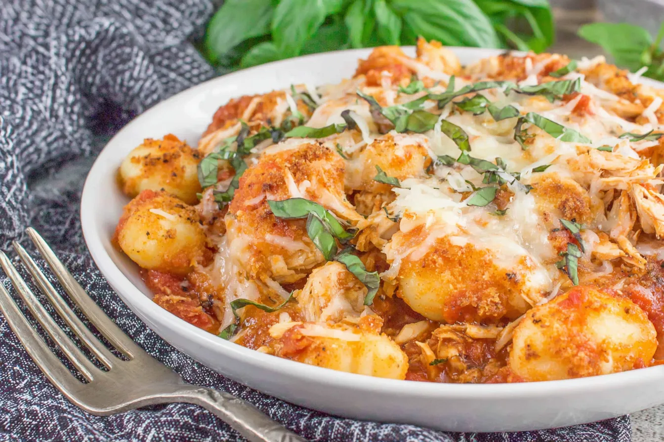 Chicken Parmesan Gnocchi served in a white bowl with melted mozzarella, shredded chicken, tomato sauce, and crispy breadcrumb topping