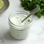 Fresh Cilantro Lime Crema in a glass jar with lime wedges and cilantro