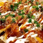 Crab Rangoon Nachos topped with creamy crab rangoon sauce, sweet-and-sour drizzle, sesame seeds, and sliced green onions on crispy chips.