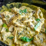 Spoonful of creamy Slow Cooker Basil Chicken Coconut Curry with shredded chicken, coconut curry sauce, and fresh basil in a crockpot.