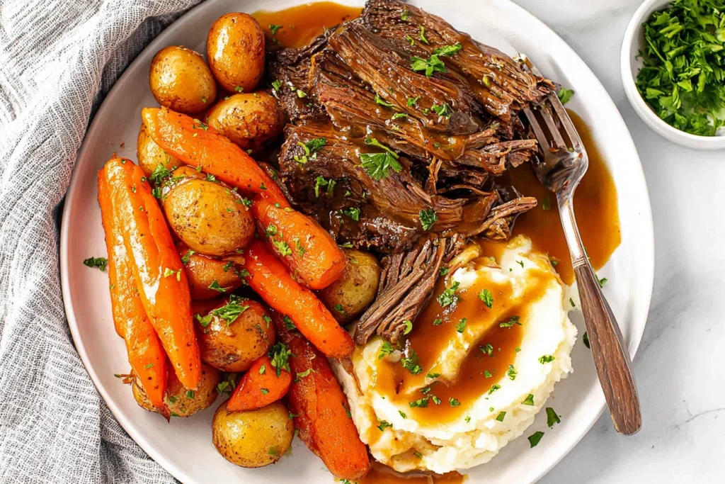 Easy Crock Pot Pot Roast plated with tender shredded beef, baby potatoes, carrots, mashed potatoes, and rich brown gravy, garnished with parsley.