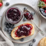 Healthy Chia Seed Jam spread on toasted bread with fresh blueberries and a glass jar on a ceramic plate