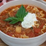 Healthy Crockpot Lasagna Soup in a white bowl with rich tomato broth, ground beef, broken lasagna noodles, ricotta on top, and fresh basil garnish.