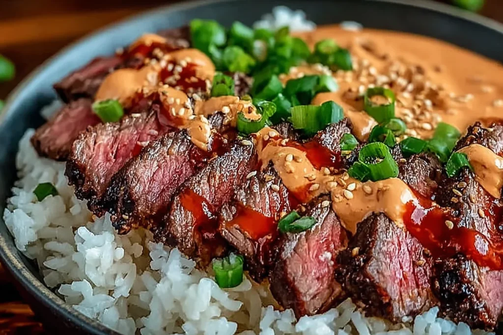Close-up of Korean BBQ Steak Rice Bowls with juicy sliced steak, jasmine rice, spicy sriracha cream sauce, sesame seeds, and fresh green onions