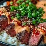 Korean BBQ Steak Rice Bowls topped with sliced medium-rare steak, jasmine rice, spicy cream sauce, sesame seeds, and green onions