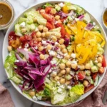 Mediterranean-Style Chopped Salad topped with chickpeas, feta, cucumbers, tomatoes, red onion, bell peppers, and oregano vinaigrette in a white bowl.