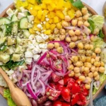 Mediterranean-Style Chopped Salad in a wooden bowl with chickpeas, feta, cucumbers, tomatoes, red onion, peppers, and oregano vinaigrette.
