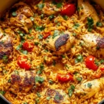 Nando’s Portuguese Chicken and Rice in a pot with fluffy golden basmati rice, charred chicken thighs, burst tomatoes, and fresh herbs.