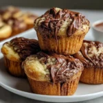 Nutella Banana Swirl Muffins stacked on a plate with rich chocolate drizzle