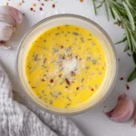 Creamy Parmesan Vinaigrette topped with herbs, garlic, and red pepper flakes in a glass bowl