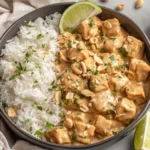 Peanut Tofu with Coconut Rice served in a bowl with creamy peanut sauce, fluffy white rice, lime wedges, and chopped peanuts