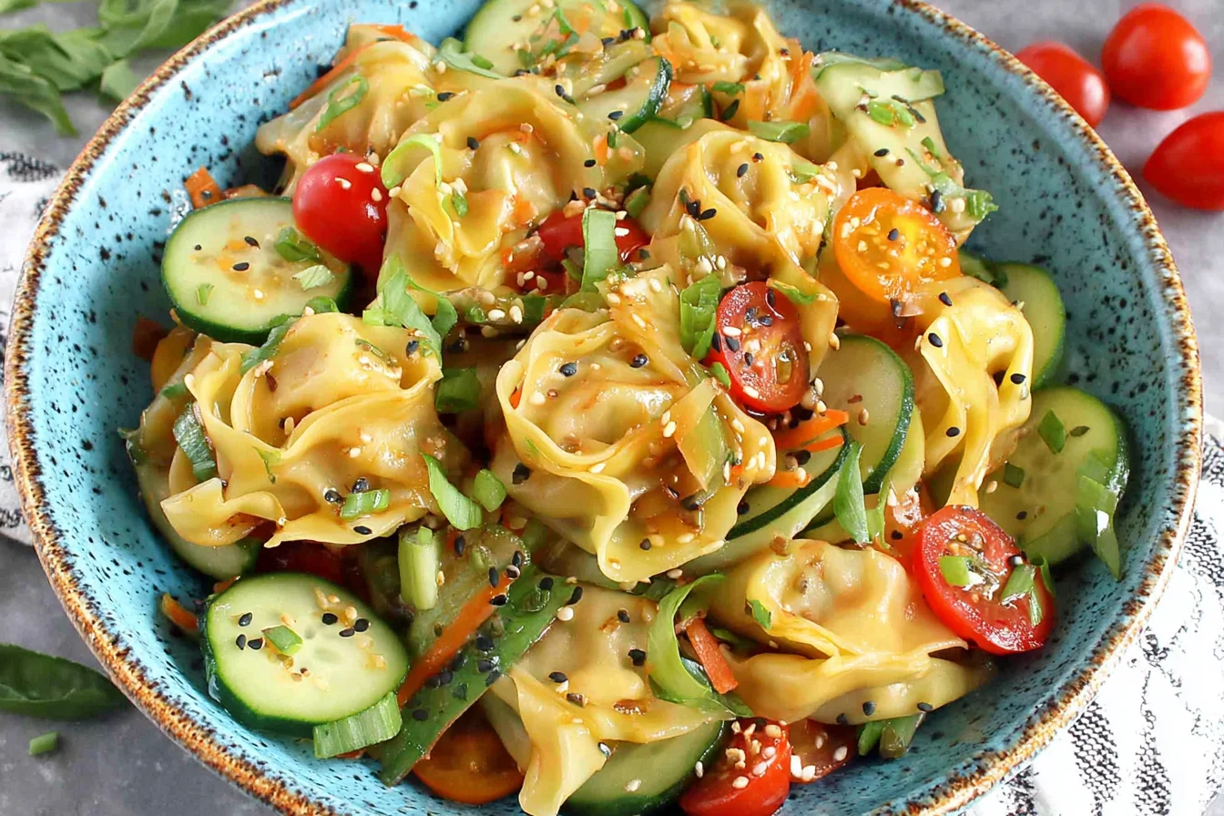Potsticker Salad Recipe in a blue bowl with steamed gyoza dumplings, sliced cucumbers, cherry tomatoes, basil, and sesame seeds.