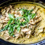 Top view of Slow Cooker Basil Chicken Coconut Curry in a crockpot, with shredded chicken in creamy coconut curry sauce topped with fresh basil.