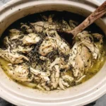 Slow Cooker Greek Chicken Recipe cooking in a crockpot with shredded lemon herb chicken, onions, and savory juices ready to serve.