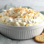 Coconut Cream Pie Dip in a white serving bowl with toasted coconut and round crackers on the side