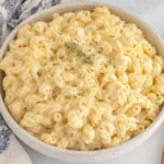 Creamy Greek Yogurt Mac and Cheese in a white bowl topped with shredded cheese and herbs