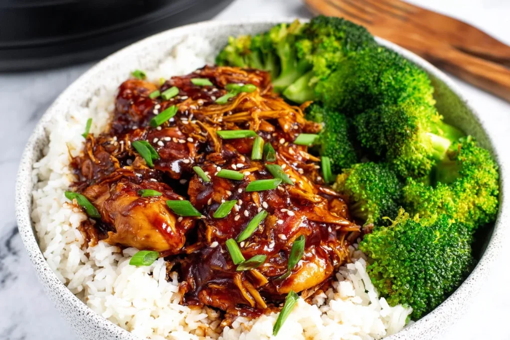 No-Fuss Slow Cooker Honey Garlic Chicken served over fluffy white rice with steamed broccoli, topped with sesame seeds and sliced green onions.